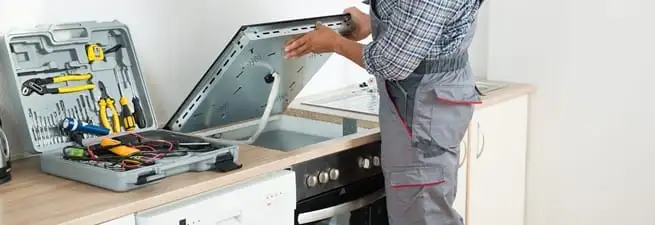 Cooktop repair technician lifting a built-in stovetop for service in Jacksonville, FL