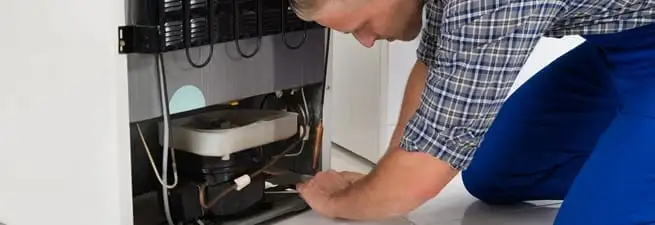 Refrigerator repair technician servicing the compressor and condenser area in Jacksonville, FL